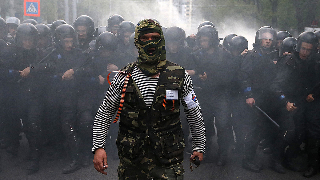 Manifestante pró-Rússia caminha na frente da polícia de choque durante uma manifestação pró-Ucrânia na cidade de Donetsk