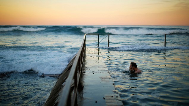 Homem lava o rosto em uma piscina à beira do Oceano Pacífico durante o entardecer em Cronulla Beach, Sydney