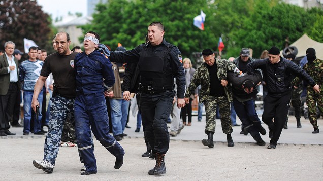 Ativistas pró-Rússia conduzem um funcionário do serviço de incêndio com os olhos vendados, para o prédio da administração regional na cidade de Donetsk, na Ucrânia