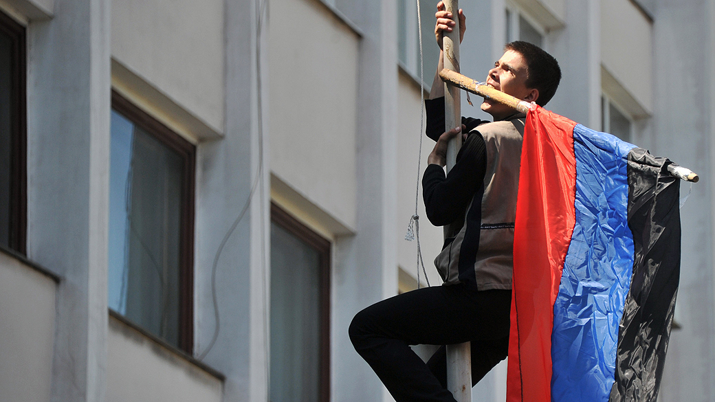 Manifestante pró-Rússia sobe no mastro com a bandeira da chamada República Donetsk, na cidade de Mariupol, na região de Donetsk