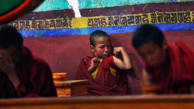 Jovem monge budista flexiona os músculos durante as orações da manhã no Mosteiro Thikse em Ladakh, na Índia