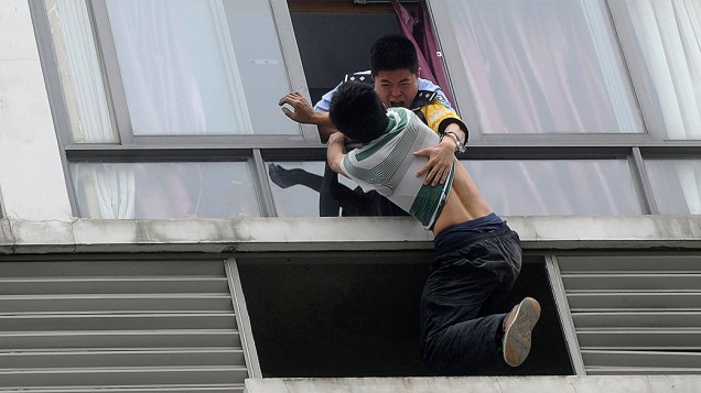 Foto divulgada na quarta-feira (21) mostra um policial resgatando um homem que tentava pular do sétimo andar de um hotel, em Chengdu, província de Sichuan, na China
