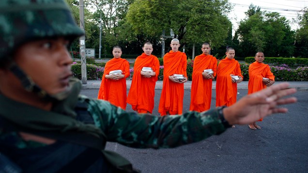 Soldado tailandês fica de guarda enquanto monges budistas esperam por doações nos arredores de um templo, em Bangcoc