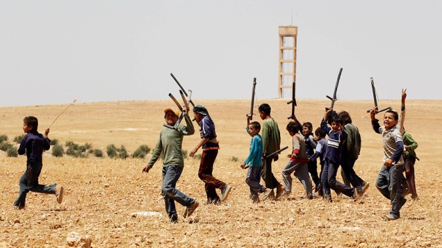 Crianças sírias cantam enquanto seguram armas de mentira durante um treinamento militar em uma área rural em Hama. A maioria delas tem parentes no Exército Sírio Livre e afirmam ter formado sua própria unidade de combate