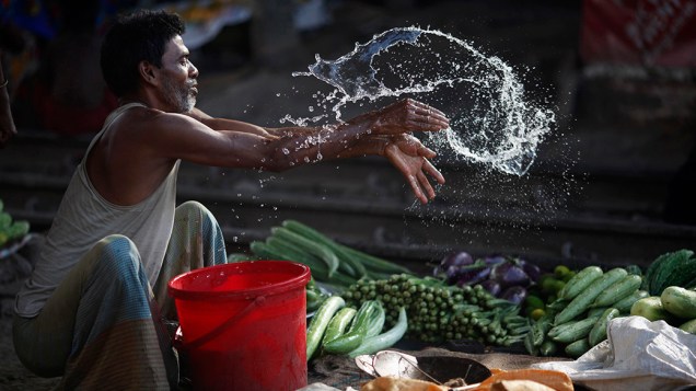 Vendedor joga àgua em vegetais em Daca, em Bangladesh