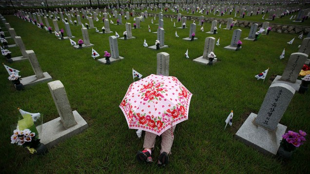 Mulher senta em frente ao túmulo de um familiar no cemitério nacional em Seul, na véspera do Dia da Memória da Coreia do Sul, que homenageia pessoas que morreram pelo país
