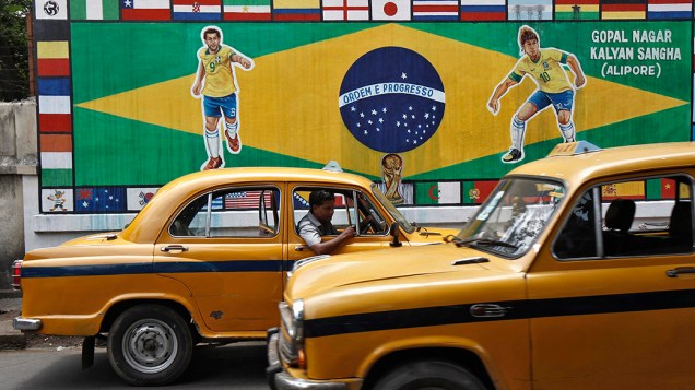Em Calcutá, táxis são vistos em frente a painel com pinturas de jogadores brasileiros e diversas bandeiras nacionais em homenagem a Copa do Mundo de Futebol de 2014