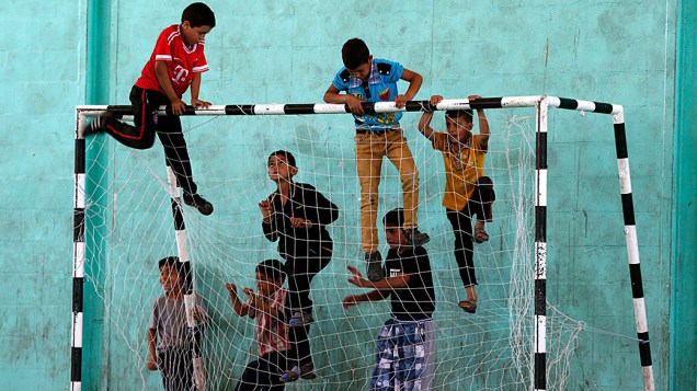 Crianças sírias e palestinas subiram em uma trave antes do início de uma partida de futebol no campo de refugiados Al-Baqaa, na Jordânia