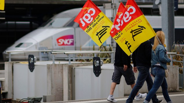 Trabalhadores da ferroviária estatal francesa continuam em greve; Na imagem, manifestantes carregam bandeiras sindicais em protesto contra as reformas previstas pelo governo