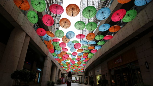 Mulher caminha sob os guarda-chuvas coloridos de uma exposição no shopping center da cidade de Kunming, na China