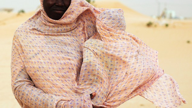 Mulher protege seu filho do vento ao andar entre as dunas em Nouakchott, na Mauritânia