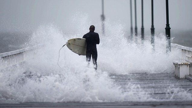 Surfista caminhou ao longo do cais durante uma tempestade em Port Phillip Bay, na cidade Melbourne, na Austrália