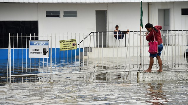 Mulher tenta atravessar uma avenida inundada durante chuvas torrenciais em Recife (PE)