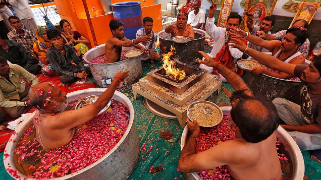 Sacerdotes hindus se sentam em caldeirões para fazer oferendas durante a realização do Parjanya Varun Yagam, oração especial para pedir chuva, na cidade Ahmedabad, na Índia