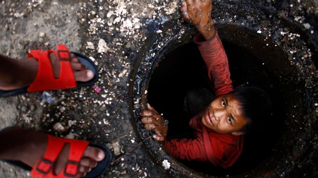 Menino sai de buraco depois de limpar manualmente um bloco de esgoto no mercado de vegetais em Katmandu, no Nepal. Crianças são usadas como mão de obra barata para limpar banheiros públicos, drenos e lixo acumulando em áreas de mercado em todo o país. Ongs internacionais vem trabalhando em conjunto pelos Direitos Humanos no Nepal