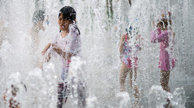 Crianças brincam em fonte para se refrescar, durante o quente verão em Xangai, na China
