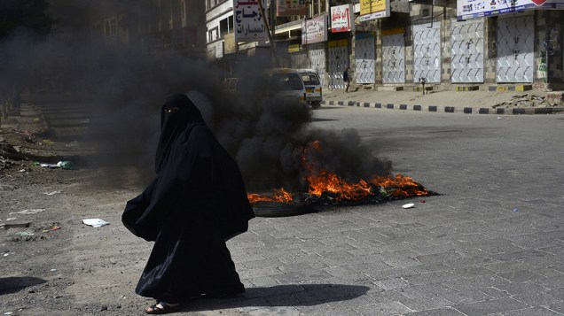 Uma mulher passa por vários pneus em chamas durante um protesto contra o aumento dos preços dos combustíveis, na cidade de Sanaa, no Iêmen