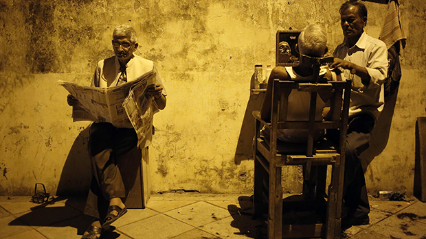 Homem aguarda para ser atendido em barbeiro de rua, em Nova Délhi, na Índia