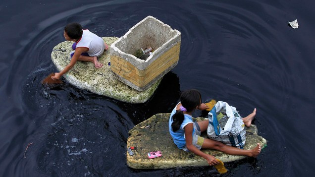 Crianças usam pedaços de isopor como barquinhos para recolher lixo plástico na Baía de Manila, nas Filipinas. O material é vendido ao equivalente a pouco mais de R$ 0,04 por quilo<br> 