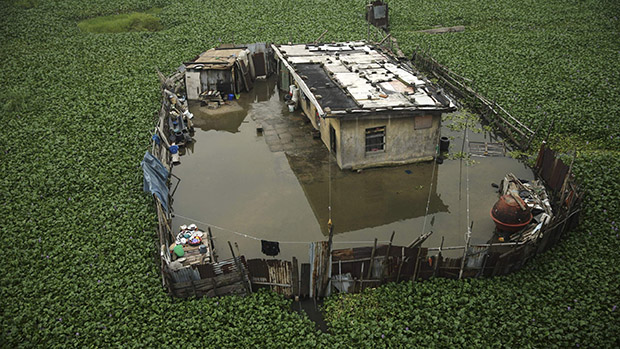 Uma casa é vista parcialmente submersa e rodeada por aguapés na beira de uma lagoa na Nigéria