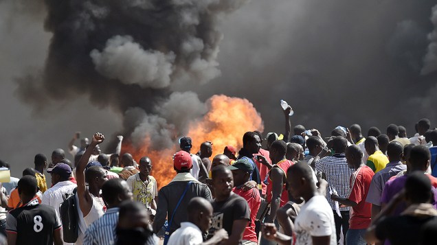 Moradores de Uagadugu, em Burkina Faso, observam fumaça depois que manifestantes atearam fogo no Parlamento do país, em protesto contra planos do presidente Blaise Compaore de estender seu mandato, que já dura 27 anos