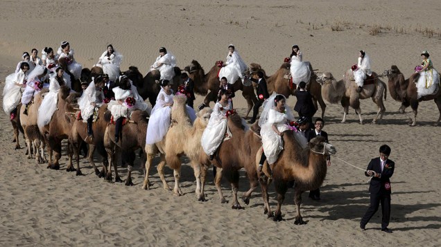 Noivos recém-casados guiam camelos levando suas esposas em uma cerimônia de casamento coletivo de 22 casais em deserto no condado de Yuli, na região autônoma de Xinjiang Uighur, na China