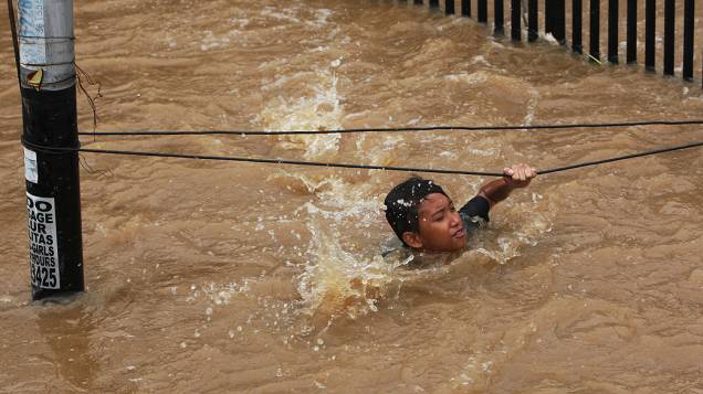 Jovem se agarra em uma corda para não ser arrastado pela água numa área inundada no distrito comercial de Jacarta (Indonésia), nesta sexta-feira (18). Pelo menos quatro pessoas morreram e milhares tiveram de deixar suas casas por causa das inundações que afetam a capital do país