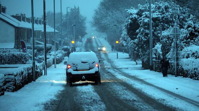 Carros ligam os faróis de manhã em Radstock, perto de Bath. Neve causa perturbação em grande parte do Reino Unido