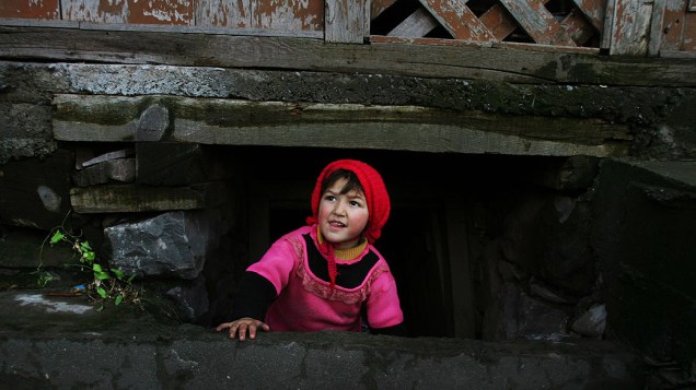 Menina é fotografada na entrada de abrigo embaixo da casa onde mora na cidade de Chakoti, na região da Caxemira, na fronteira entre o Paquistão e a Índia