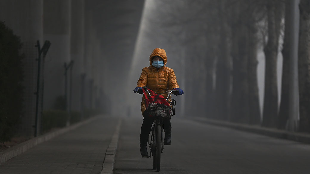 Mulher anda de bicicleta usando máscara durante forte poluição em Pequim, China