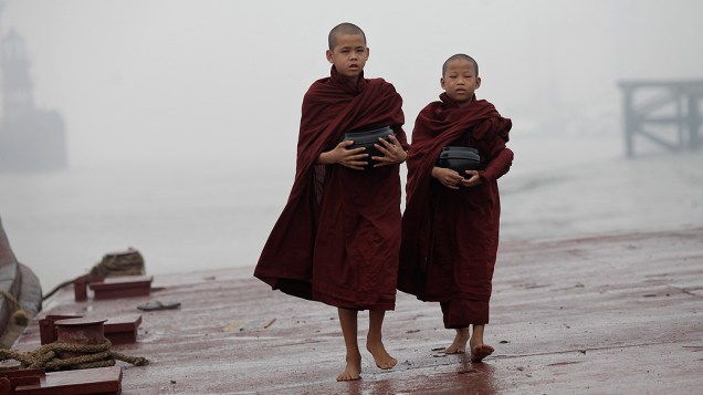 Jovens budistas caminham nas margens do rio durante manhã de forte névoa em Yangon (Mianmar)