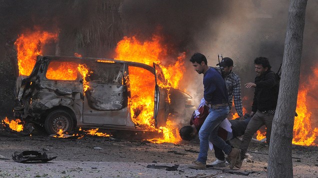 Guardas de segurança sírios carregam um corpo passando por carros em chamas no centro de Damasco, na Síria. Pelo menos 31 morreram na explosão de carro-bomba contra a sede do partido do ditador sírio, Bashar Assad