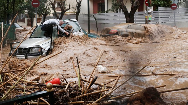 Mulher é resgatada por um morador em cima de seu carro durante inundação em Chalandri, Grécia
