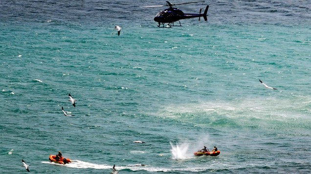 Policiais em barco inflável disparam tiros na água durante tentativa de acertar tubarão que matou um banhista na praia de Muriwai, em Aucklandna Nova Zelândia
