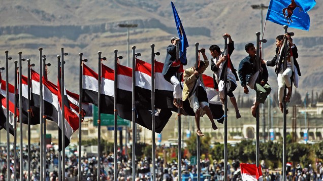 Iemenitas escalam postes em área de Sanaa, durante manifestação para comemorar o aniversário da renúncia do presidente Ali Abdullah Saleh
