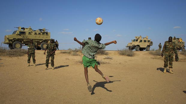 Menino joga futebol com soldados ugandenses da Missão da União Africana na Somália (AMISOM), na cidade de Buur-Hakba, na Somália