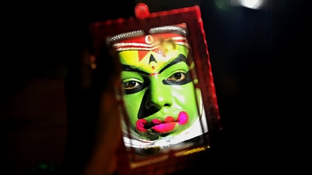Um artista tradicional coloca a maquiagem antes de um evento, na Índia