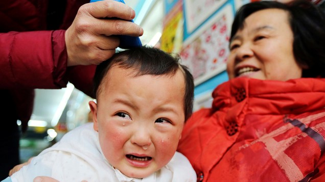 Criança chora durante corte de cabelo. Chineses acreditam que cortar mexa de cabelo de criança no 2º dia do 2º mês no calendário lunar traz sorte o ano todo