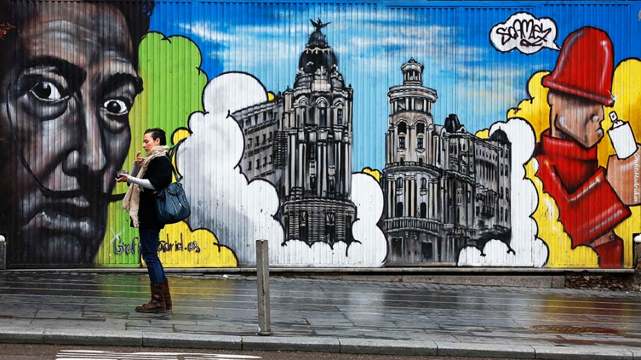 Mulher fuma em frente à um mural com grafites de arte em Madrid, na Espanha
