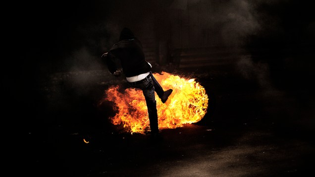 Palestino chuta um pneu em chamas durante confronto com soldados israelenses na cidade de Hebron, Cisjordânia