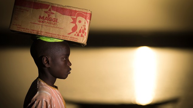 Menino carrega uma caixa em sua cabeça próximo ao rio Níger, em Gao, no Mali