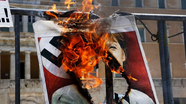 Cartaz com a foto da chanceler alemã, Angela Merkel vestindo um uniforme nazista é incendiado por um manifestante em frente ao parlamento grego na Praça Syntagma, em Atenas 