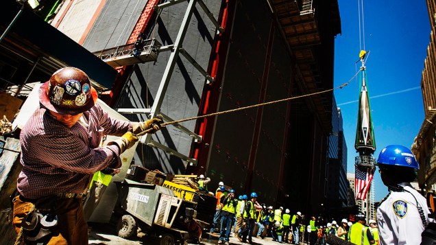Trabalhador usa uma linha para firmar a peça final de um pináculo com a bandeira dos Estados Unidos antes de ser colocada  no topo do One World Trade Center, em Nova York