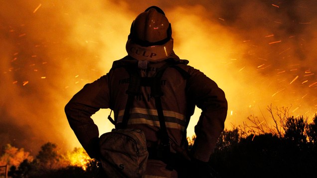 Bombeiro monitora a ação para conter incêndio florestal ao longo da costa da Califórnia ao norte de Los Angeles. O incêndio levou a evacuação de centenas de casas e um campus universitário, nos Estados Unidos