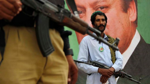 Policial e segurança particular perto do retrato de Nawaz Sharif, líder do partido Liga Muçulmana do Paquistão-Nawaz (PML-N), durante um comício de campanha eleitoral em Peshawar. As eleições gerais do Paquistão serão realizadas no dia 11 de maio