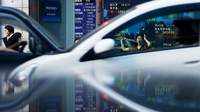 Pedestres passam por uma placa eletrônica mostrando os preços das ações de vários países, visto através das janelas do carro em Tóquio