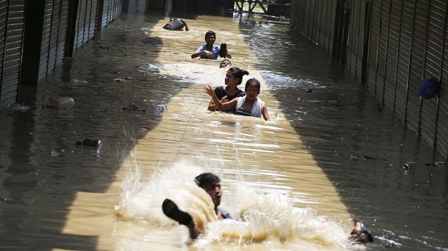 Moradores tentam por uma rua inundada situada ao longo do rio Yamuna, em Nova Delhi, Índia. Devido as fortes chuvas o número de mortes chegou a 142 e 500 desaparecidas nas últimas horas