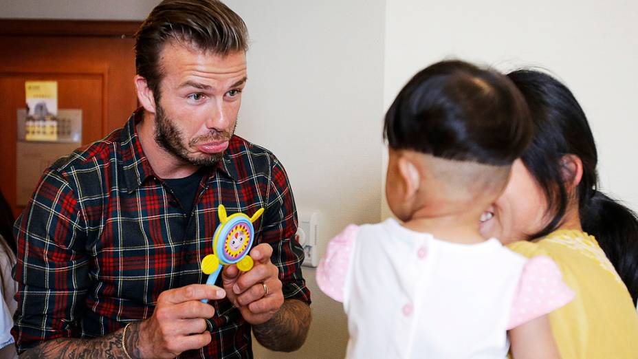 O ex-capitão da seleção inglesa de futebol, David Beckham brinca com uma criança que sofre de doença cardíaca congênita, durante uma visita a um hospital em Hangzhou, província de Zhejiang, na China