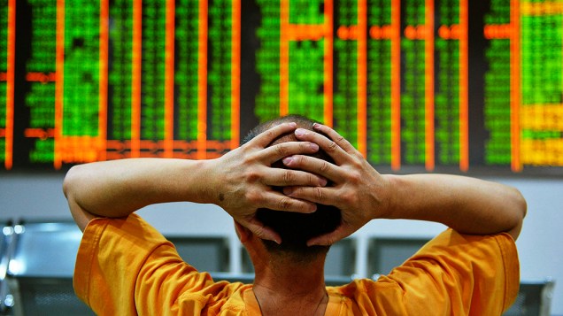 Investidor se senta na frente de um painel eletrônico que mostra informações sobre ações em uma corretora em Hangzhou, província de Zhejiang, na China