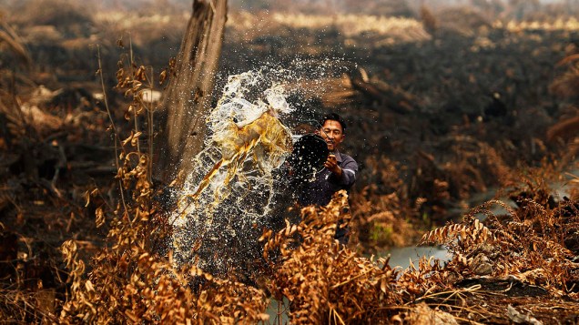 Trabalhador joga água para apagar um incêndio que está queimando sua plantação de abacaxi, em Rokan Hilir, na Indonésia